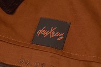 deuXros jacket close-up of leather patch label and date detail at chest pocket, brown cotton canvas